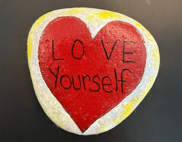 Stone with heart painted on it with text Love Yourself inside heart
